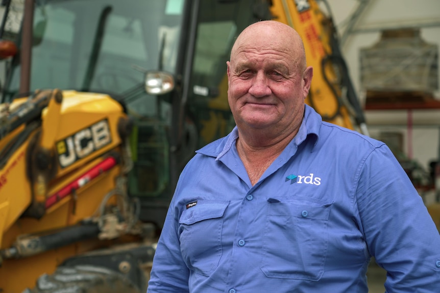 A man wearing a blue shirt standing in front of a bulldozer.