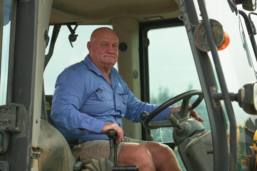 A man wearing a blue shirt behind the wheel of a bulldozer.