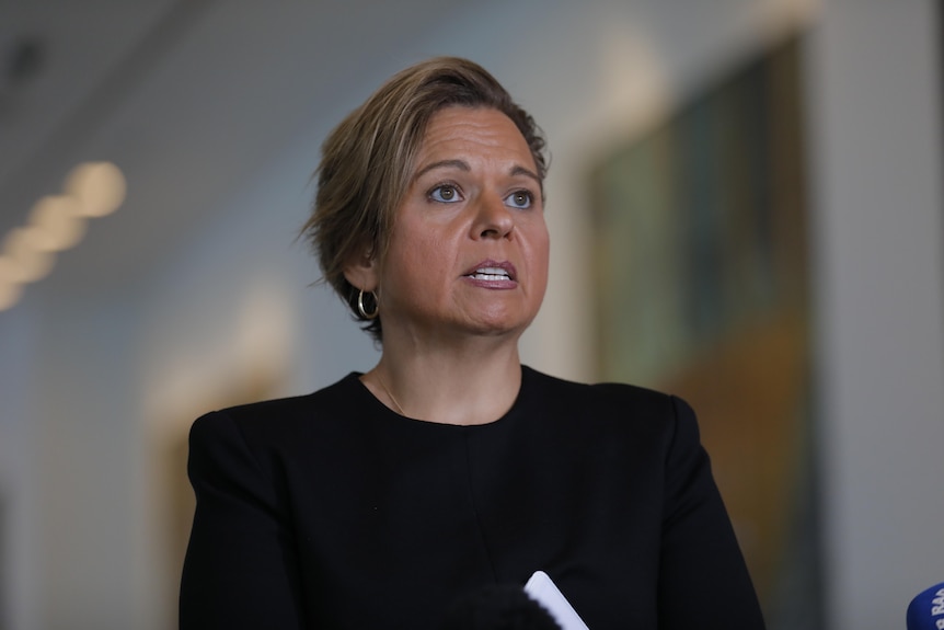 A woman with short hair and a black top, speaking.