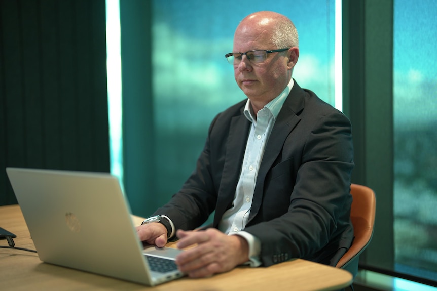 A man wearing glasses, a collared shirt and suit jacket, typing on a laptop.