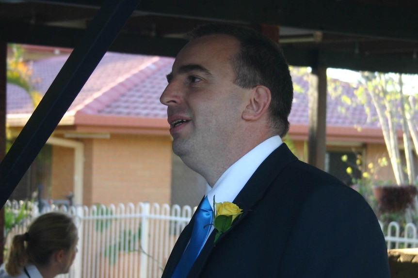 A man wearing a suit and tie and a flower in his jacket button hole.